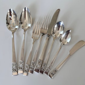 May include: A set of eight silver-plated flatware pieces, including a butter knife, a serving spoon, a slotted spoon, and five forks. The flatware has an ornate design with a floral pattern.