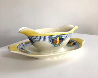 May include: Cream-colored gravy boat and matching saucer with yellow and blue accents. The rim of the boat and the edges of the saucer are yellow. The boat and saucer feature a blue and white striped pattern and a floral design.