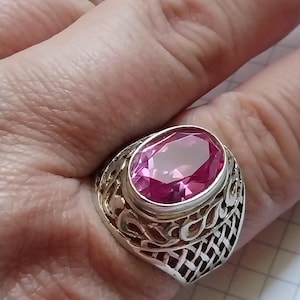Pode incluir: Um anel de prata com um design ornamentado e uma grande gema oval rosa.