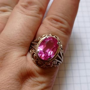 Può includere: Un anello d'argento con una grande pietra preziosa rosa di forma ovale incastonata in un delicato design a filigrana.