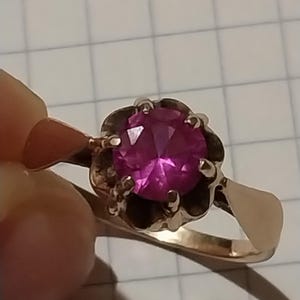 以下が含まれることがあります： 装飾的な金のセッティングにセットされた、大きなファセットカットのピンクの宝石が付いた金のリングです。