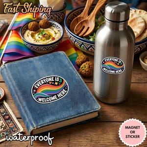 Puede incluir: Una botella de agua de acero inoxidable y un libro cubierto de mezclilla presentan cada uno una pegatina con un diseño de arcoíris y el texto "Everyone is Welcome Here". La imagen también incluye una pegatina rosa que dice "Magnet or Sticker".