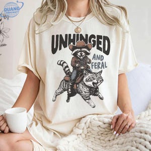 Unhinged and Feral Comfort Colors Shirt, Funny Raccoon Western Tee,Cowboy Raccoon Riding a Cat Shirt, Snarky Saying Graphic T-Shirt,Racoon