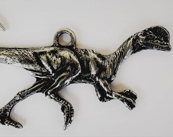 May include: A silver-colored dinosaur charm with a long neck and tail. The dinosaur is in a running pose with its mouth open. The charm has a loop at the top for attaching to a necklace or bracelet.