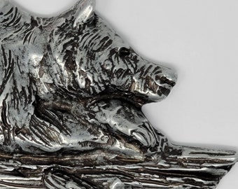 May include: A silver-toned bear sculpture, with a detailed, textured finish, is perched on a log. The bear's head is turned to the side, and its paws are visible.