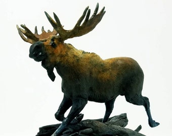 May include: A bronze sculpture of a moose with large antlers, standing on a wooden base with a green and brown base. The moose is depicted in a running pose with its head turned to the side.