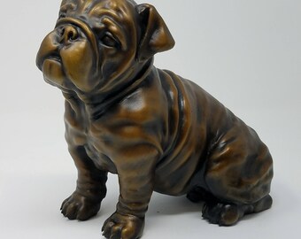 May include: A bronze bulldog figurine sitting with its head tilted to the side. The figurine is detailed with realistic features and a textured finish.