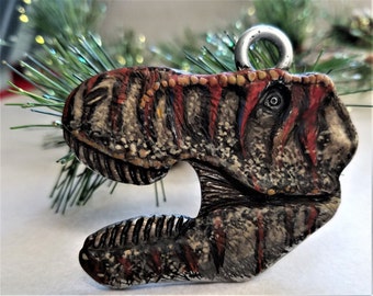 May include: A hand-painted dinosaur ornament with a red, brown, and white color scheme. The ornament has a loop at the top for hanging on a Christmas tree.