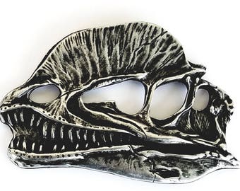May include: A silver-colored dinosaur skull pendant with detailed features, including teeth and eye sockets.