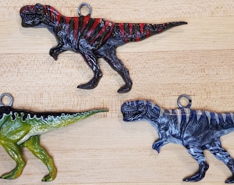 May include: Three dinosaur ornaments, each painted in a different color scheme. The first dinosaur is black with red stripes, the second is green with black stripes, and the third is blue with white stripes.