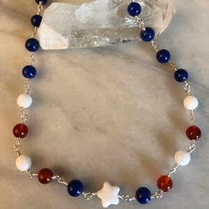 May include: A necklace made with blue, white, and orange beads, with a white star charm in the center.