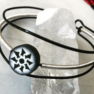May include: A black and silver double-strand bracelet with a black and white circular charm featuring a geometric design.