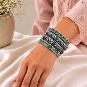May include: A set of four stacked bracelets featuring a dark oxidised metal finish and smooth, round, light green cabochon stones. The bracelets are arranged in a row on the wrist, showcasing a consistent design of alternating metal and stone.