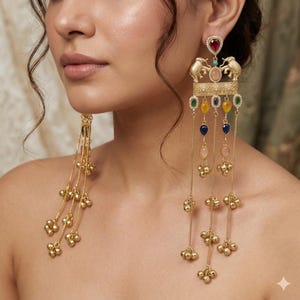 May include: Gold-toned earrings with intricate detailing. Each earring features a decorative top with elephant figures and colorful gemstones. Long chains with dangling gold beads and gemstone drops add movement and flair to the design.