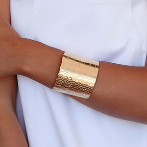 May include: A gold necklace with a turquoise bead chain and five gold leaf pendants. The necklace is worn by a person with a white sleeveless dress and a gold bracelet on their wrist.