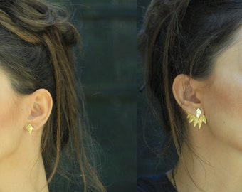 May include: A woman with long brown hair is wearing a pair of gold leaf earrings. The earrings are a delicate design with multiple small leaves.