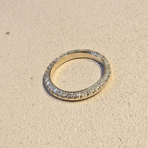 Puede incluir: Un fino anillo de banda de oro con una fila de pequeños diamantes que rodean la banda.