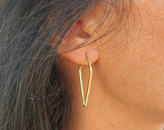 May include: Gold triangle shaped hoop earrings. The earrings are worn by a person with long dark hair.