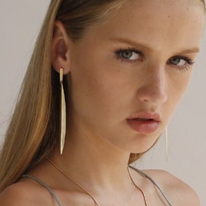 Puede incluir: Una mujer con un vestido de satén plateado, un collar y pendientes de oro. También lleva un brazalete de oro en el brazo.