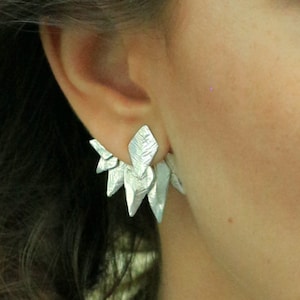 May include: Silver earrings with a geometric, leaf-like design. The earrings are made of multiple small, pointed pieces that create a cluster effect.