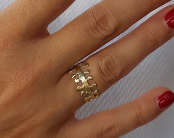 Könnte beinhalten: Ein goldener Ring mit einem einzigartigen, strukturierten Design. Der Ring wird am Ringfinger einer Hand mit rotem Nagellack getragen.