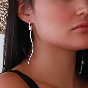 Puede incluir: Una mujer con un sombrero de paja con una banda blanca y un top negro sin mangas. Lleva pendientes largos de plata.