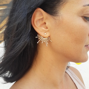 May include: Gold ear cuff earrings with a sunburst design. The earrings are made of metal and have a shiny finish.