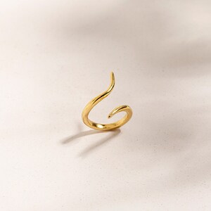 May include: A gold-toned ring with a unique, twisted design. The ring is open and has a pointed end.