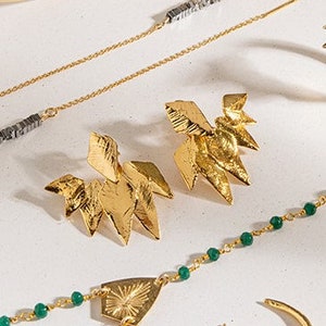 May include: A set of gold jewelry featuring geometric shapes, including earrings, a necklace, and a bracelet. The earrings are large and angular, while the necklace and bracelet feature smaller, more delicate shapes. The jewelry is made of gold metal and has a polished finish.