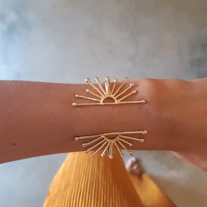 K&ouml;nnte beinhalten: Goldenes Sonnenstrahlen-Armband mit einem zarten Design. Das Armband ist offen und verstellbar, um an die meisten Handgelenke zu passen.