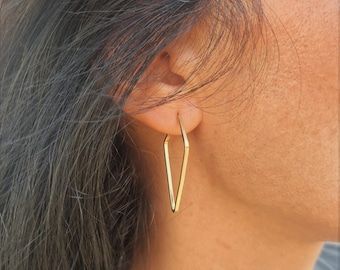 May include: Gold triangle shaped hoop earrings. The earrings are worn by a person with long dark hair.