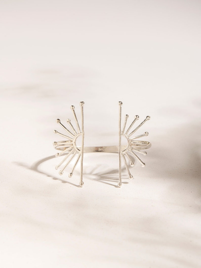 K&ouml;nnte beinhalten: Ein silbernes Armband mit einem Sonnenstrahlen-Design. Das Armband ist an beiden Seiten offen und hat eine zarte, luftige Ausstrahlung.