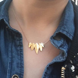 May include: A gold necklace with a geometric pendant made of multiple pointed shapes. The necklace is worn by a person wearing a denim shirt.