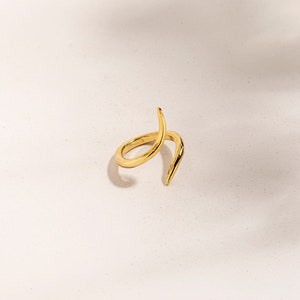May include: A gold-toned ring with a twisted, pointed design. The ring is made of metal and has a simple, modern aesthetic.