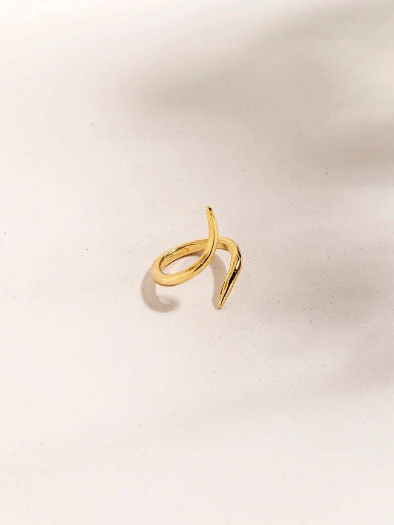 May include: A gold-toned ring with a twisted, pointed design. The ring is made of metal and has a simple, modern aesthetic.