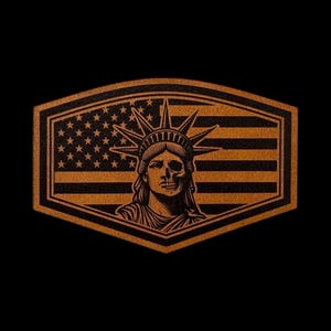 May include: A hexagonal patch featuring a copper-colored graphic of the Statue of Liberty with a skull face overlay. The background displays a stylized American flag with stars and stripes. The design is rendered in dark brown and copper tones.