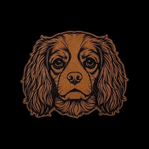 May include: A brown, textured leather-like patch featuring a detailed, engraved illustration of a Cavalier King Charles Spaniel dog face. The design showcases intricate linework highlighting the dog's long, wavy ears and expressive eyes.