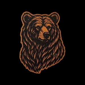 May include: A patch featuring a detailed illustration of a bear head. The design uses a high-contrast color scheme with deep black fur textures and warm, light brown highlights that define the bear's facial features, ears, and thick neck fur.