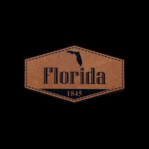 May include: A brown leather patch with the word "Florida" in bold letters and the year "1845" below. A black outline of the state of Florida is above the word "Florida". The patch has a stitched border.