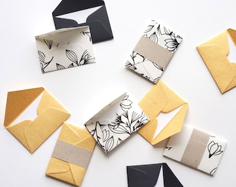 May include: A collection of small envelopes in various colors and patterns, including black, white, and gold. The envelopes are decorated with floral designs and are perfect for sending notes or small gifts.
