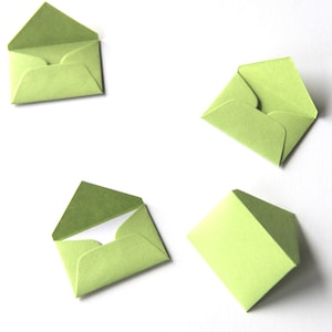 May include: Four green paper envelopes of different sizes and shapes, lying flat on a white surface.