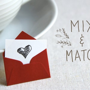 May include: A red envelope with a white card inside. The card has a hand-drawn black heart on it. The text "MIX & MATCH" is written in black on a white background.