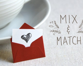 May include: A red envelope with a white card inside. The card has a hand-drawn black heart on it. The text "MIX & MATCH" is written in black on a white background.