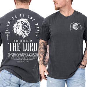 May include: Dark gray t-shirt with a white lion graphic and text that reads "Blessed is the man who trusts in the Lord." The back of the shirt features the same design with additional text from Jeremiah 17:7-8.
