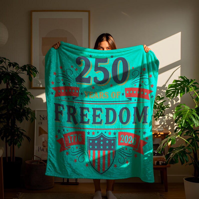A woman is holding a large turquoise blanket that displays the text "250 YEARS OF FREEDOM" and "1776" on it.