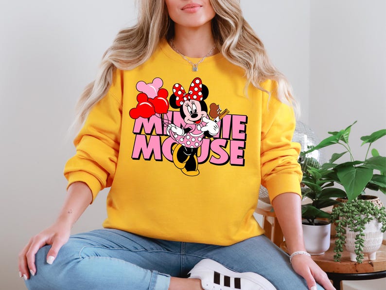 A woman wearing a yellow sweatshirt with a Minnie Mouse graphic on it, sitting in a relaxed position.