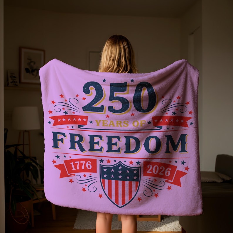 A person is holding a large pink blanket with the text "250 YEARS OF FREEDOM" and "1776" printed on it.