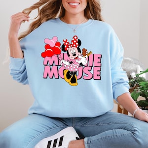 A woman wearing a light blue sweatshirt with a Minnie Mouse graphic and the text "Minnie Mouse" printed on it.
