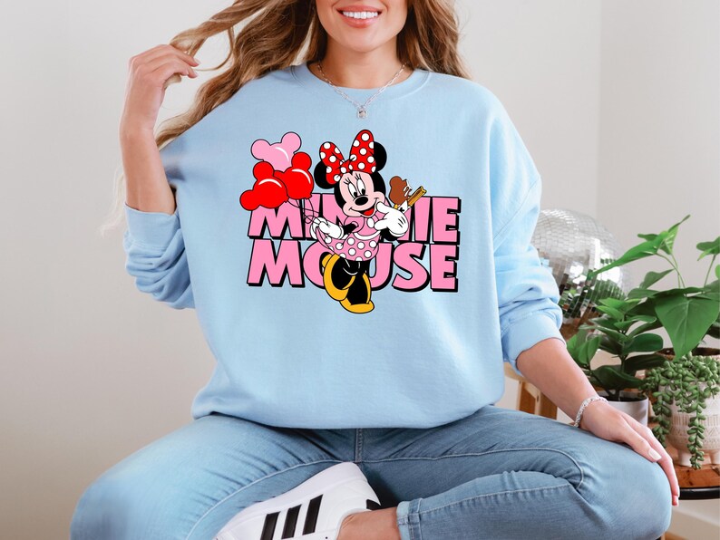 A woman wearing a light blue sweatshirt with a Minnie Mouse graphic and the text "Minnie Mouse" printed on it.