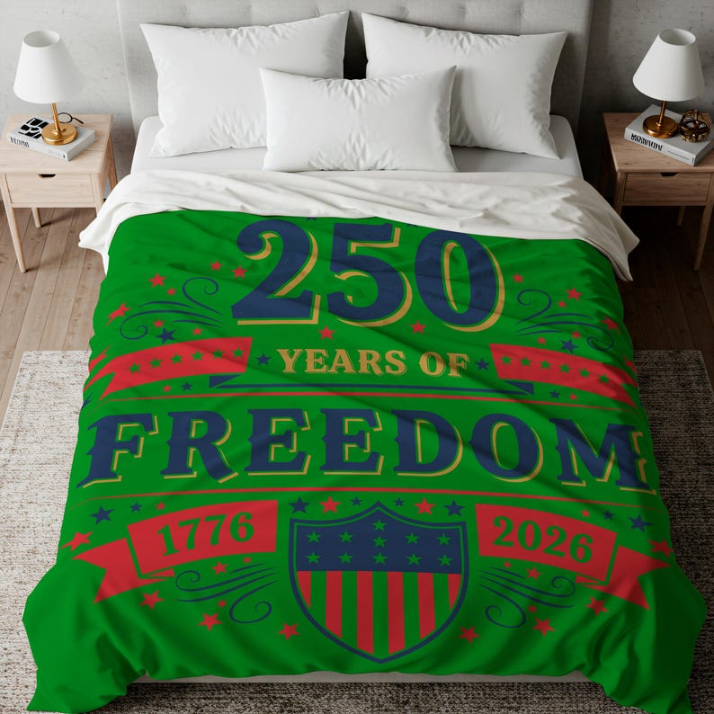 a bed with a green comforter that has a large text design celebrating the 250th anniversary of the United States.